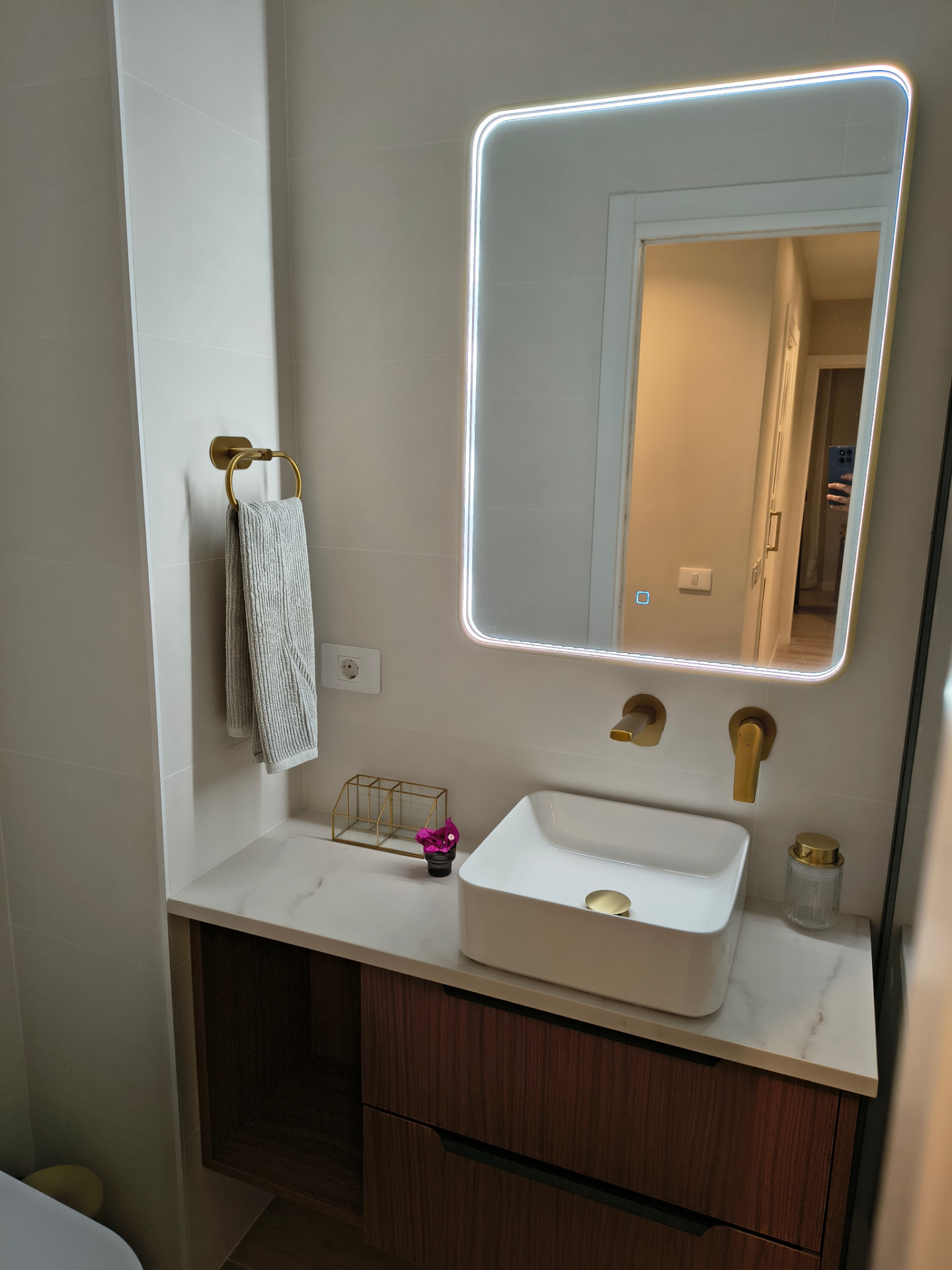 Lavabo sobre encimera marmórea con espejo retroiluminado y grifería dorada