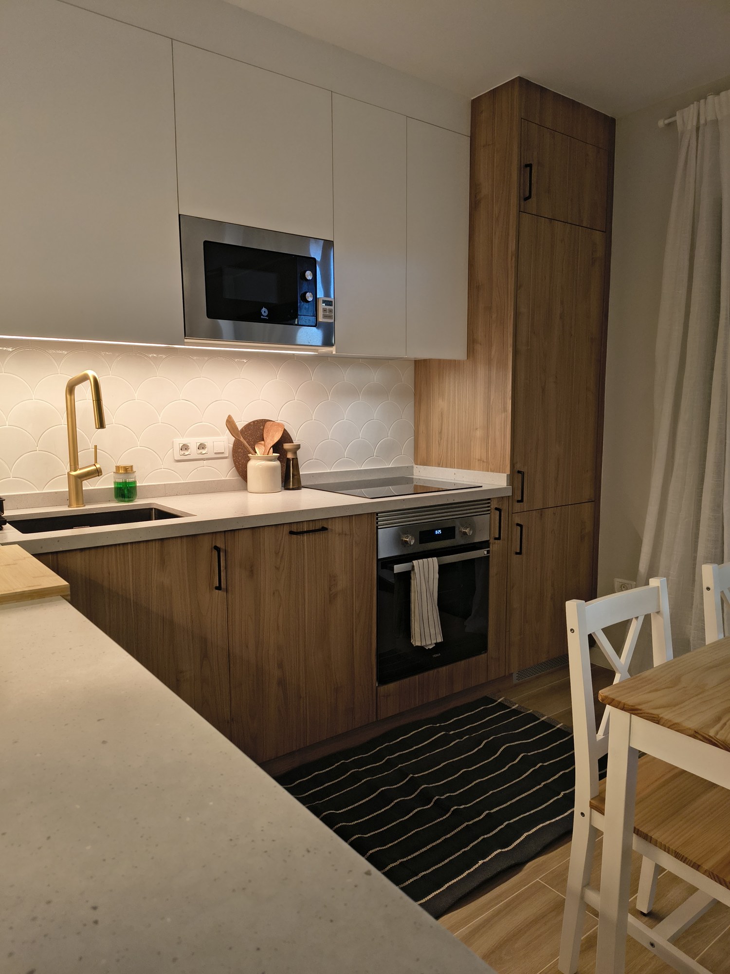 Cocina blanca en L con encimera clara e iluminación bajo los altos