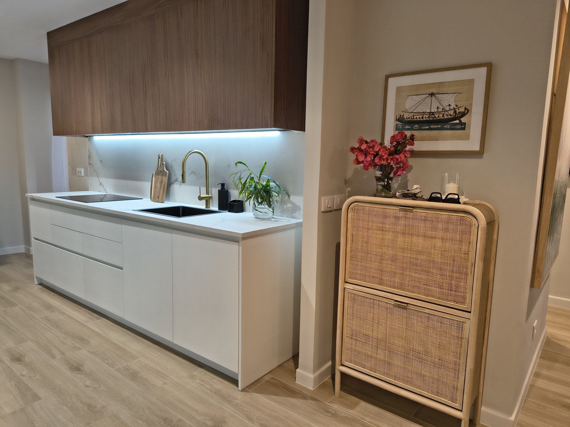 Cocina blanca con grifería dorada y mueble auxiliar de ratán