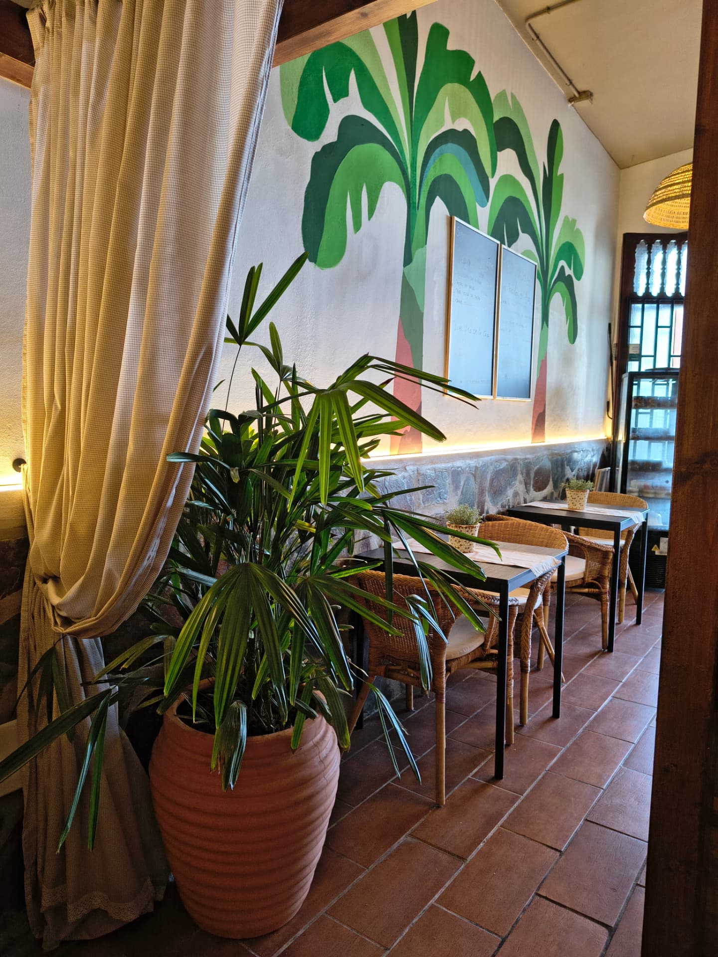 Comedor de restaurante con mural de plataneras, sillas de fibra y suelo de barro