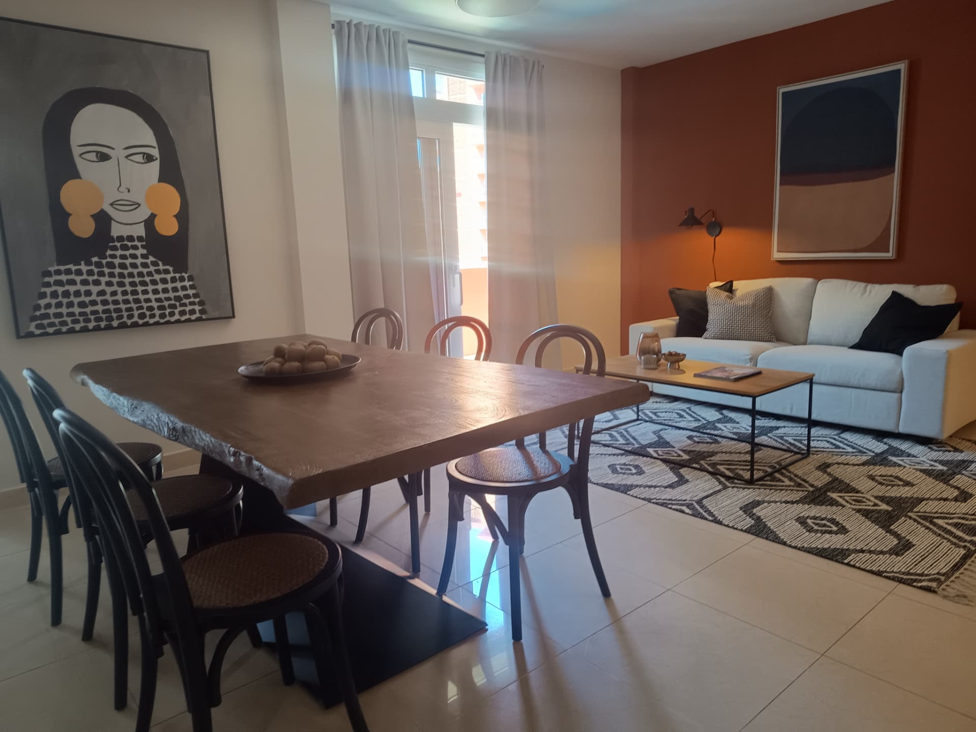 Salón comedor con mesa de madera maciza, sillas negras y pared en terracota