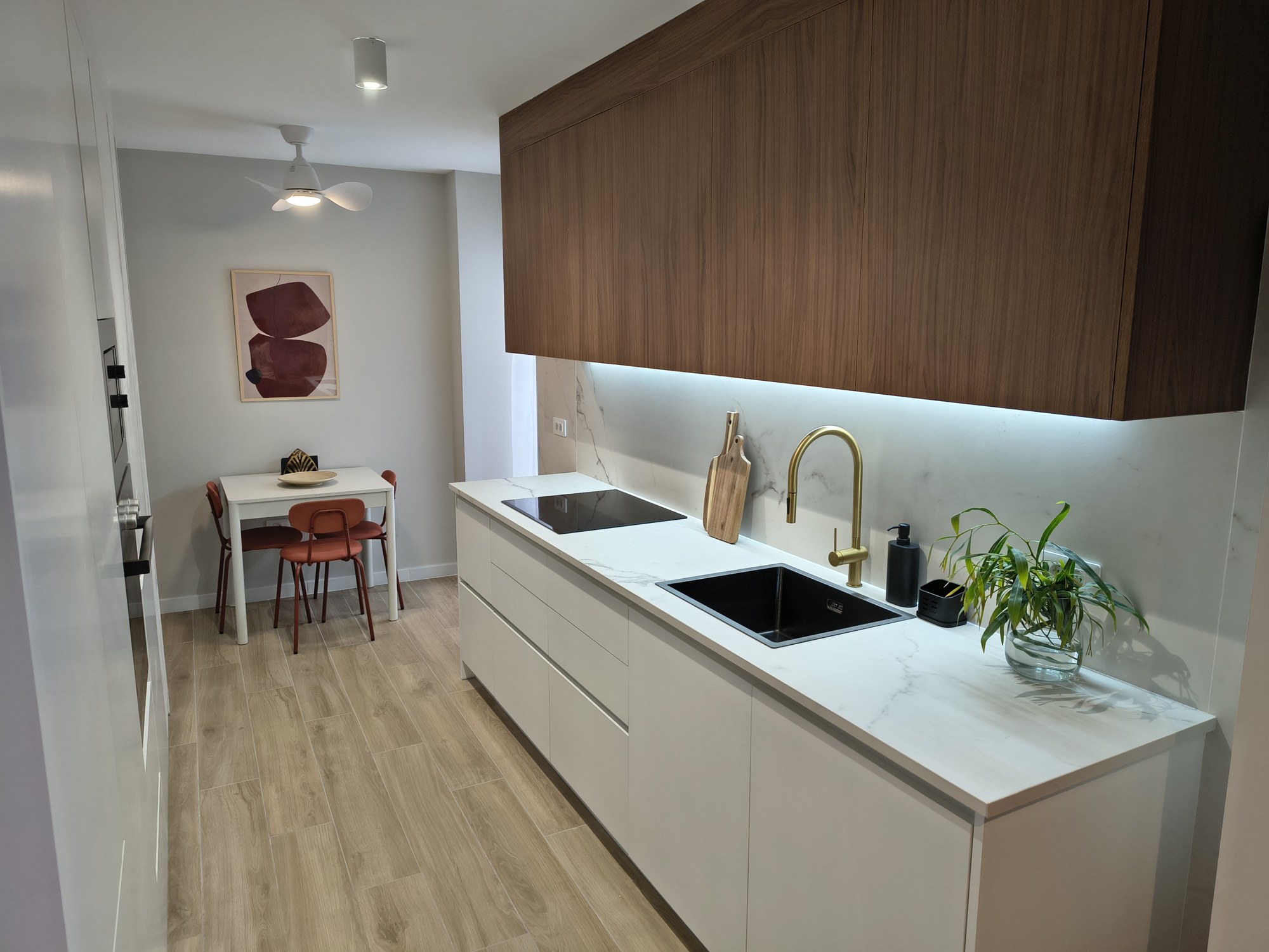 Cocina lineal blanca con office y suelo porcelánico tipo madera