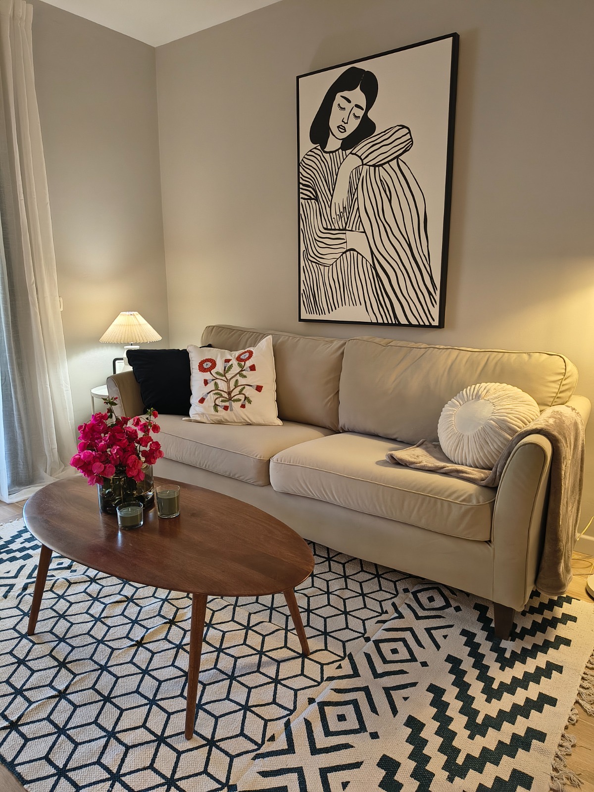 Salón reformado con sofá beige, alfombra geométrica y lámina enmarcada