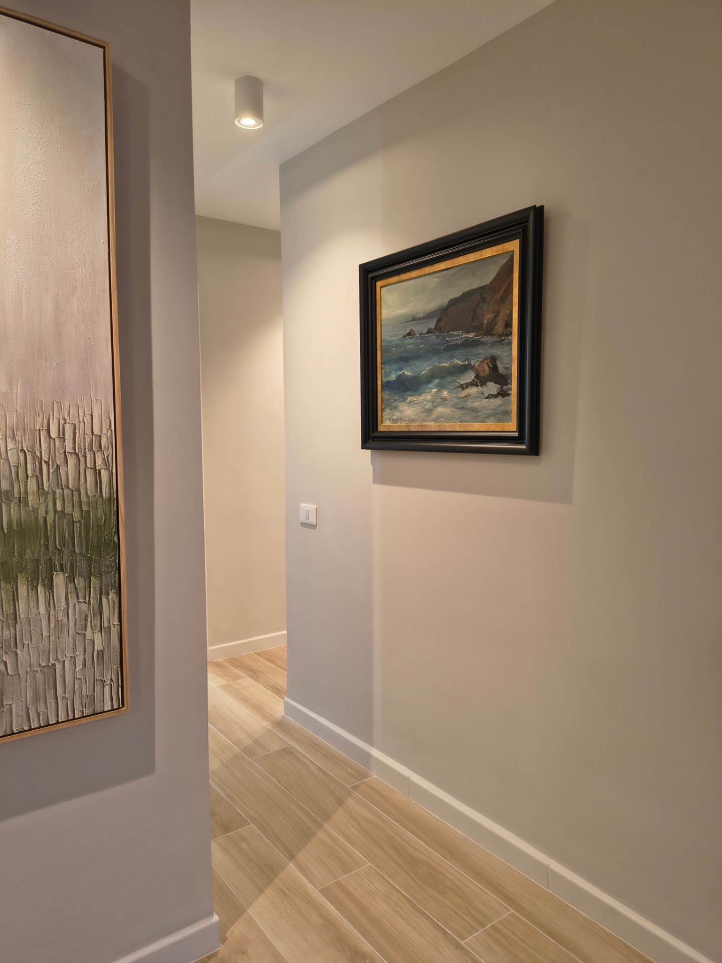 Pasillo con obra textural, marina enmarcada y suelo porcelánico tipo madera