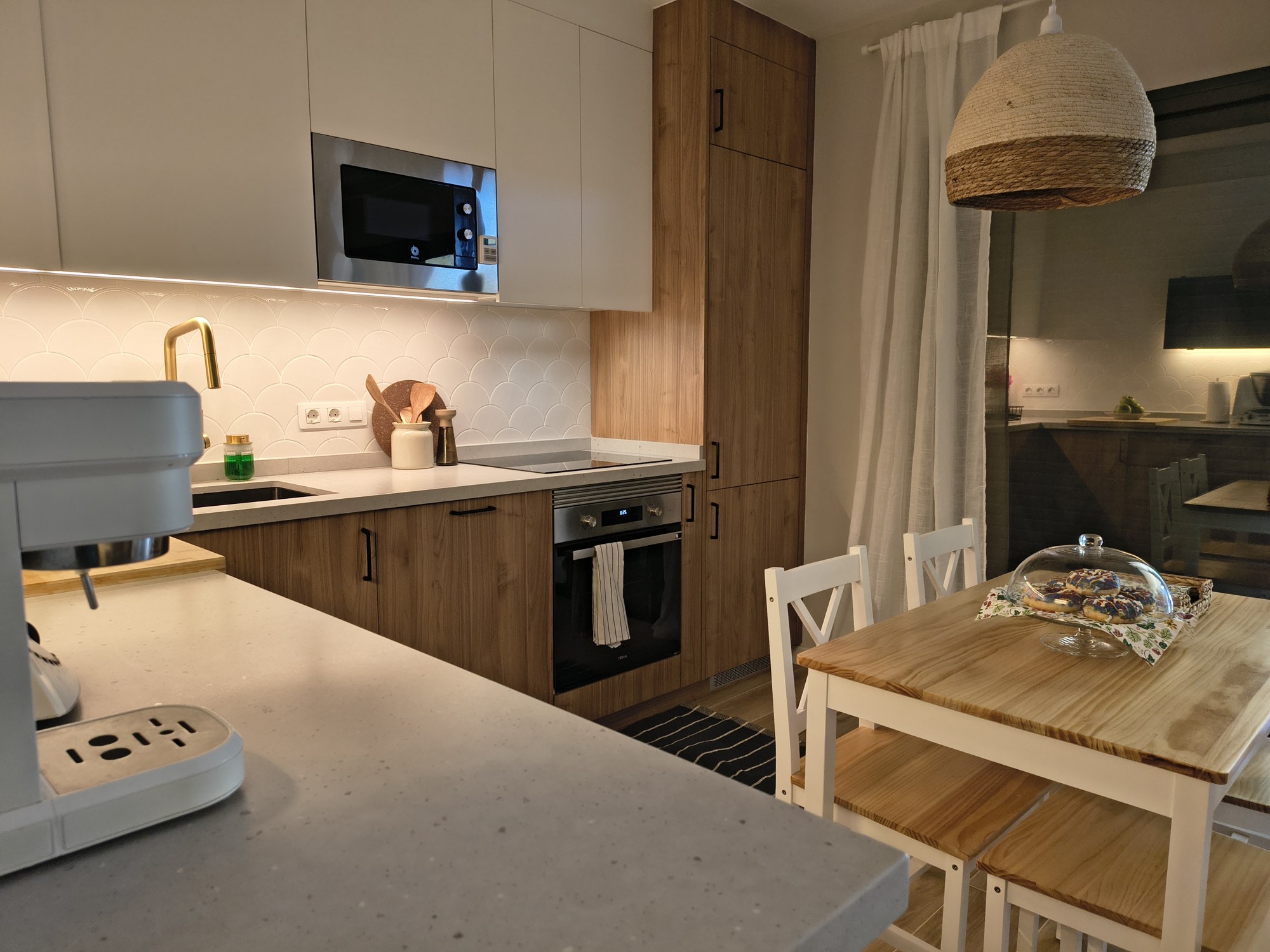 Cocina compacta con frentes de madera y zona de comedor junto a la ventana
